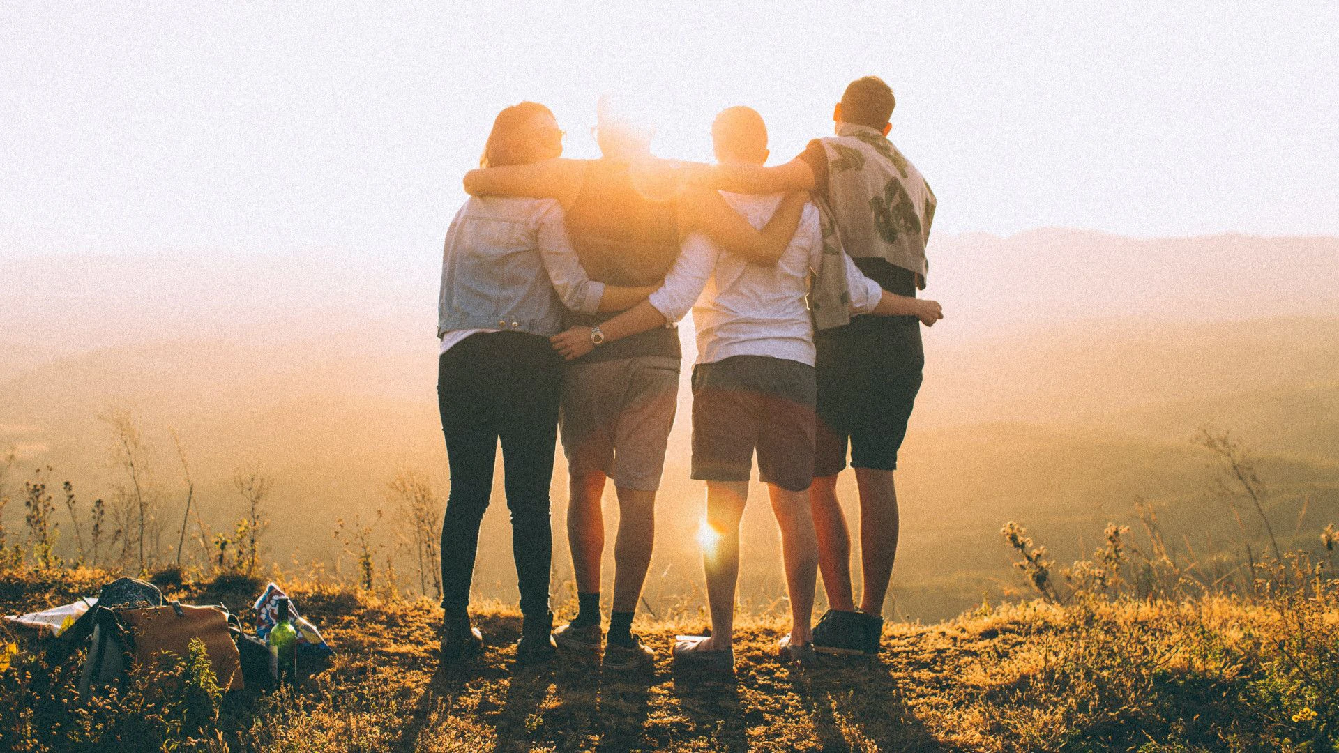 Four young people with their arms around each other watching the sunset from a viewpoint.